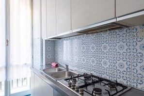 A kitchen with a gas stove, stainless steel sink, and blue patterned backsplash.