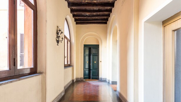 Un pasillo con piso de espiga, vigas de madera en el techo y una puerta verde al final.