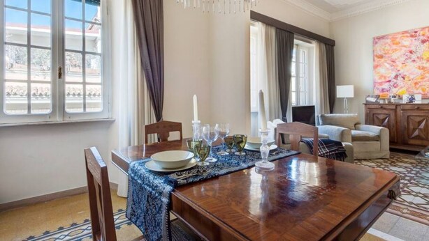 A dining area with a wooden table, chairs, a chandelier, and a view of the outside.