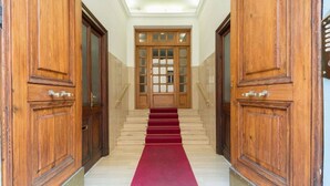 A hallway with wooden doors, a red carpet, and a staircase leading to a door with glass panels.