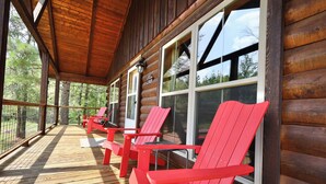 Een houten terras met rode Adirondack-stoelen en een overdekte veranda.