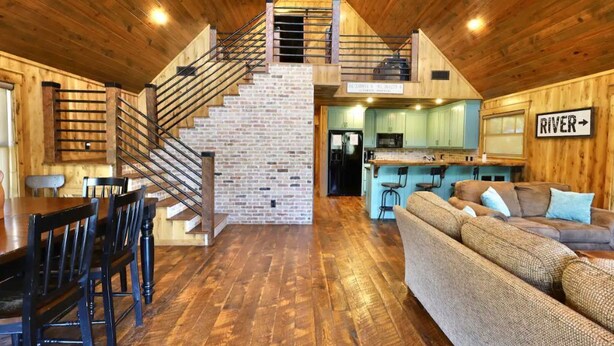 Een rustiek interieur van een chalet met een houten trap, een eethoek, een keuken en een woonkamer met een bank.