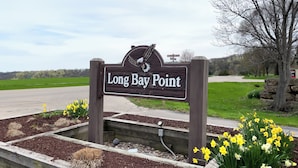 En skylt med texten ”Long Bay Point” och en örn som emblem, omgiven av blomsterrabatter och en stenkonstruktion.