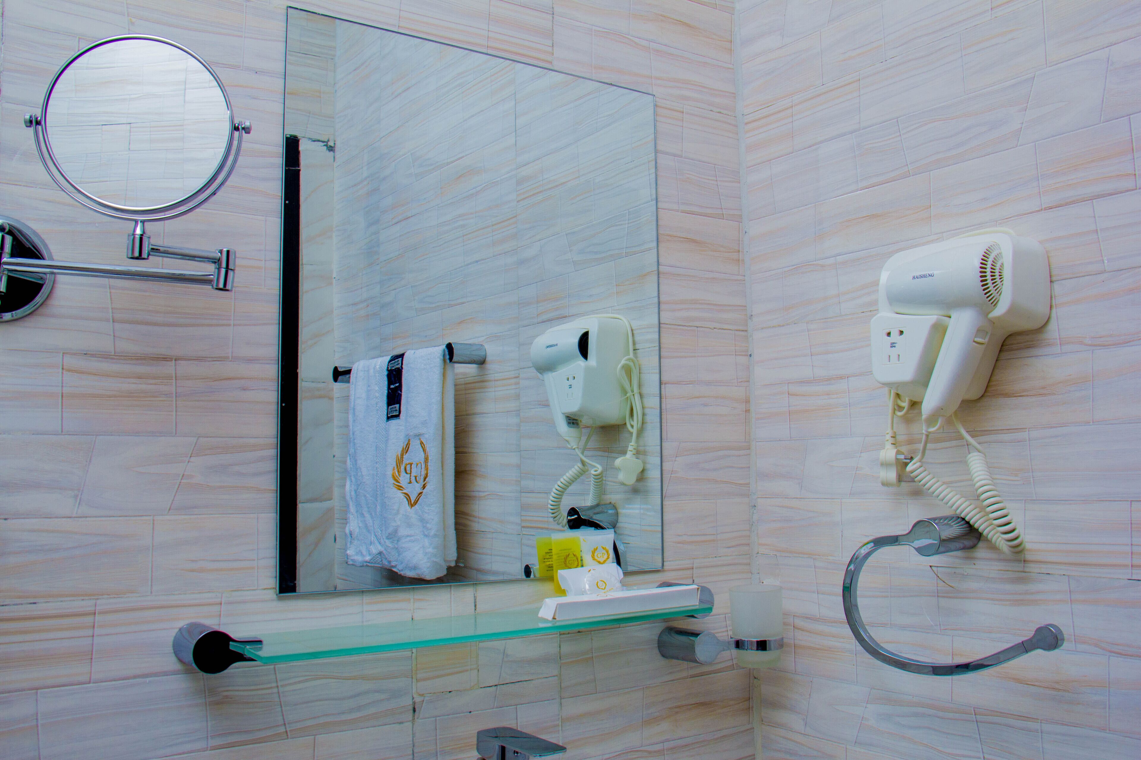 A bathroom with a mirror, towel rack, hairdryer, and a glass shelf.