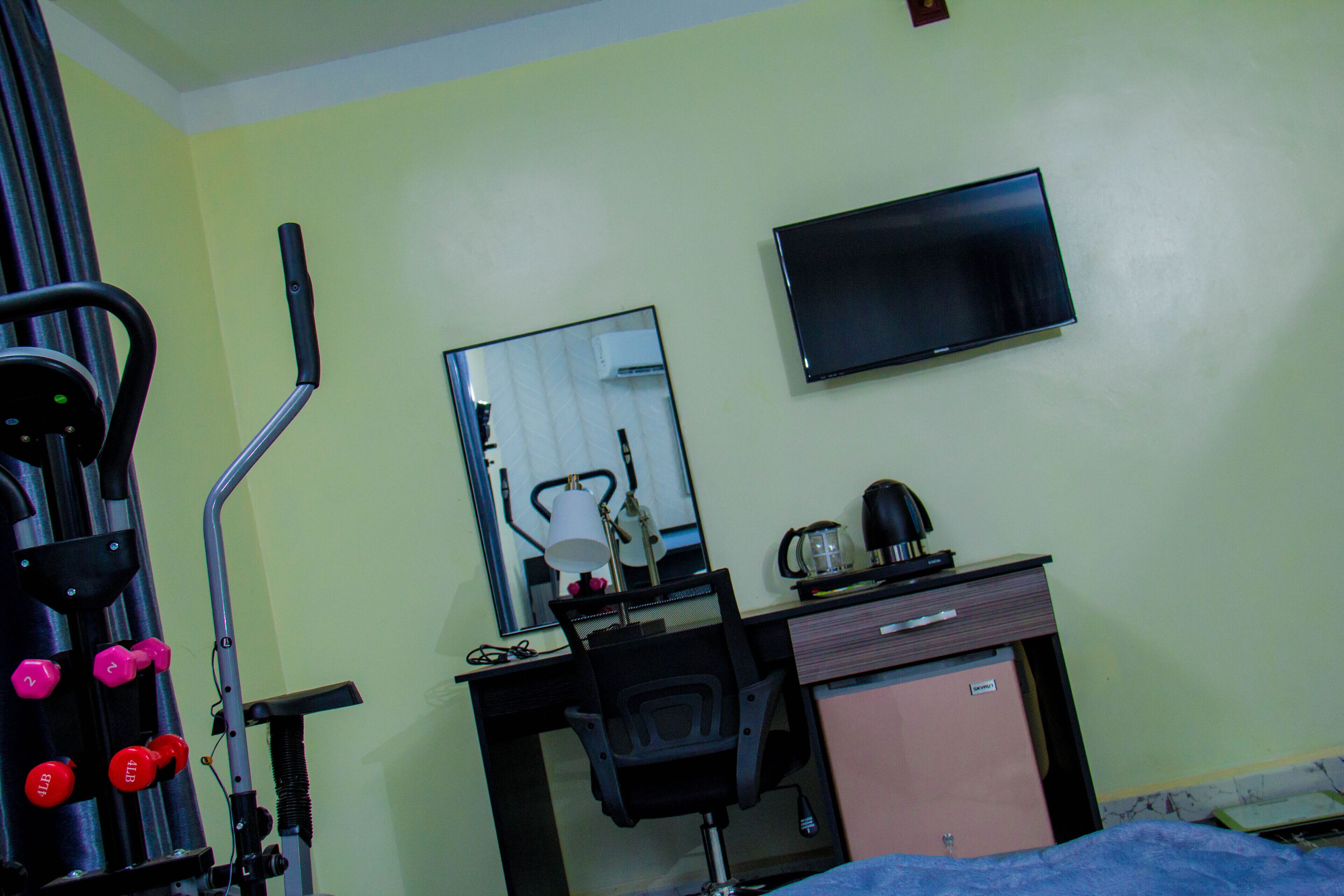 A hotel room with a desk, a television, a mirror, and exercise equipment.