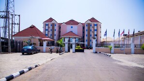 A multi-story hotel with a central entrance, a parking area, and a flag display. - GPinnacle Suites (Ilorin)