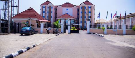 A multi-story hotel with a central entrance, a parking area, and a flag display.