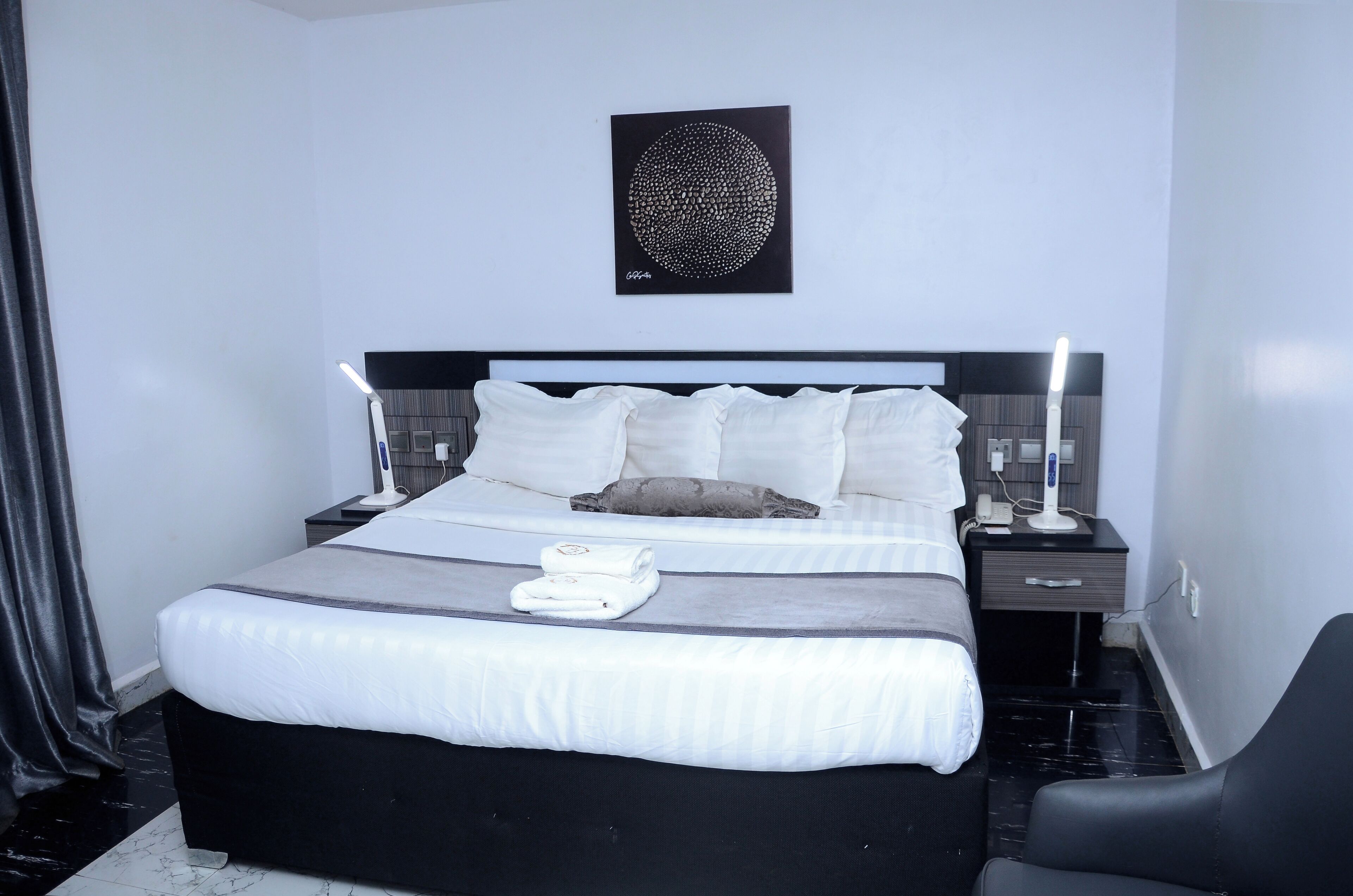 A neatly made bed with white linens, a black headboard, and a wall-mounted artwork.