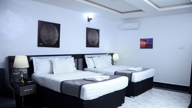 A hotel room with two beds, a desk with a lamp, and artwork on the walls. - GPinnacle Suites (Ilorin)