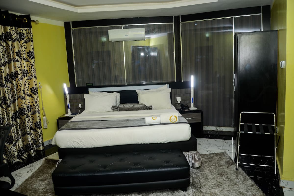 A modern hotel room with a large bed, a bedside table, an air conditioning unit, and a black wardrobe.