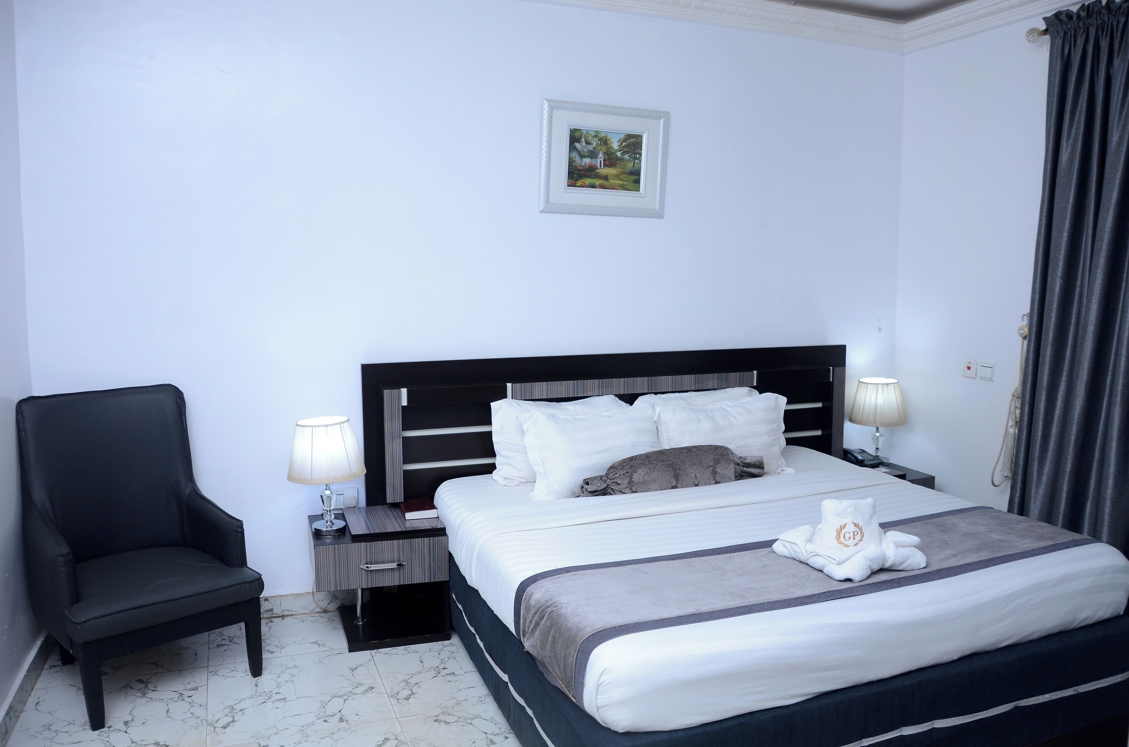 A hotel room with a large bed, a black armchair, two bedside tables with lamps, and a framed picture on the wall.