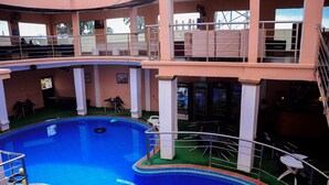 An indoor swimming pool with a surrounding deck, a bar area, and a seating area with tables and chairs. - GPinnacle Suites (Ilorin)