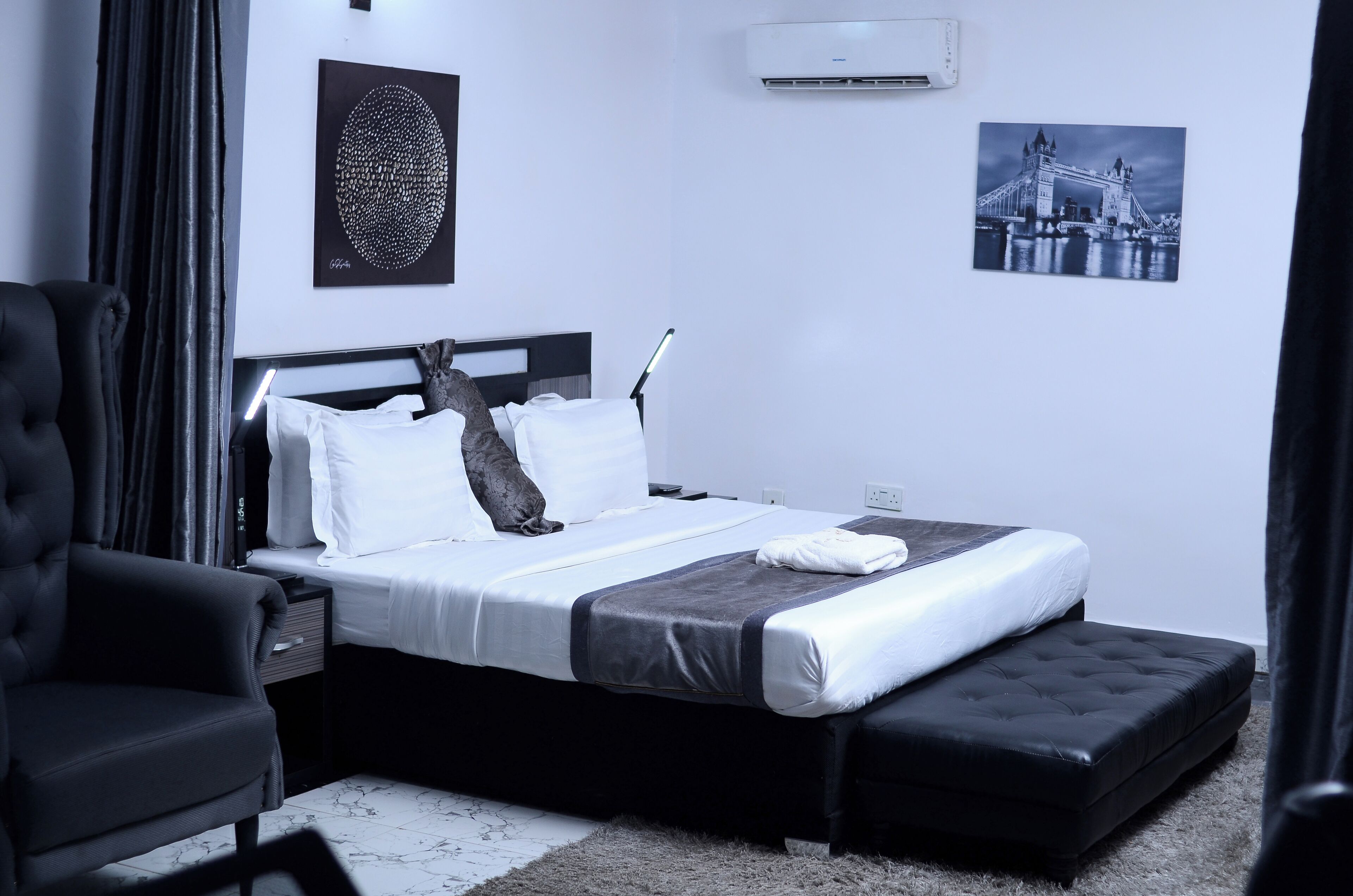 Una habitación de hotel moderna con una cama grande, un sillón negro y aire acondicionado instalado en la pared.