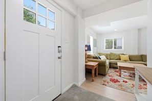 Una habitación con una puerta blanca, un sofá, una mesita y un tapete floral.