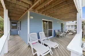 A covered deck with two white lounge chairs, a picnic table, and a sliding glass door. - 1712 - Happy Childhood, Corolla Coastal Home | Pool, Hot Tub & Game Room (Corolla)