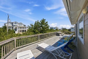A wooden deck with lounge chairs and a picnic table, overlooking a residential area with houses and trees.