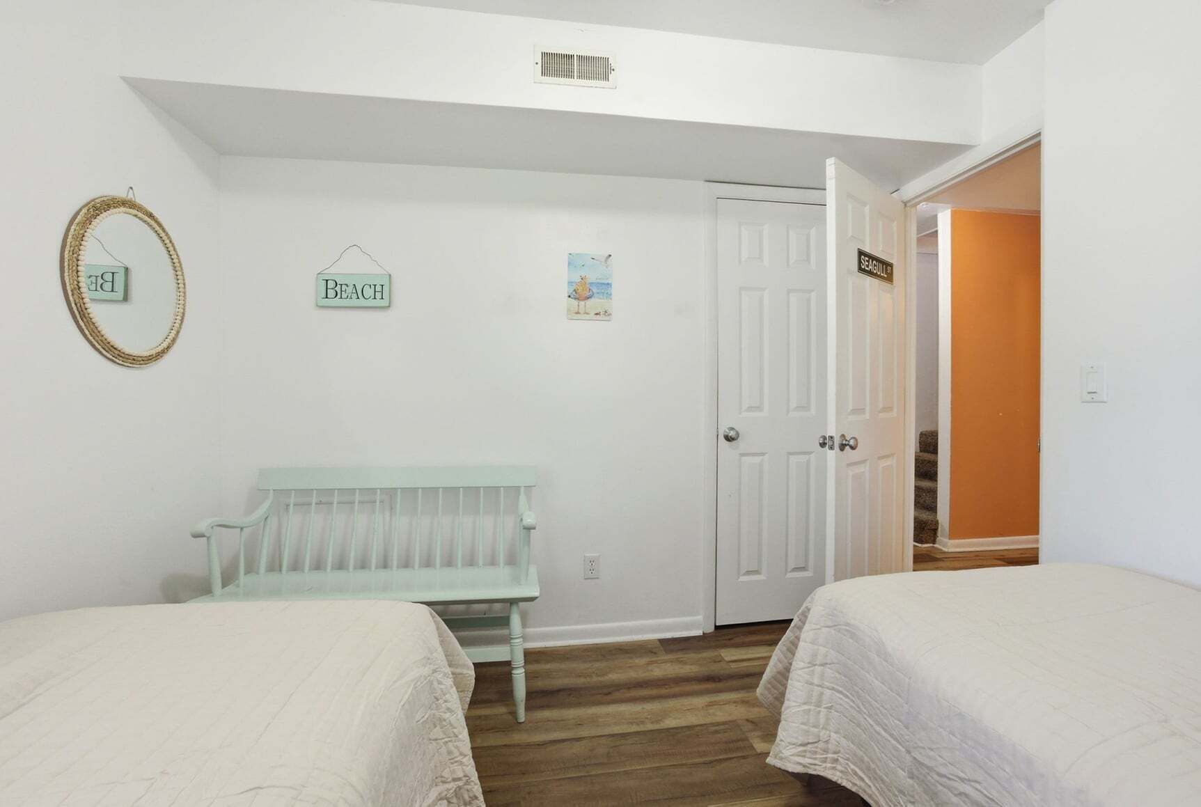 Un dormitorio con dos camas, un banco, una puerta con la etiqueta 'SEAGULL' y un cartel en la pared que dice 'PLAYA'.