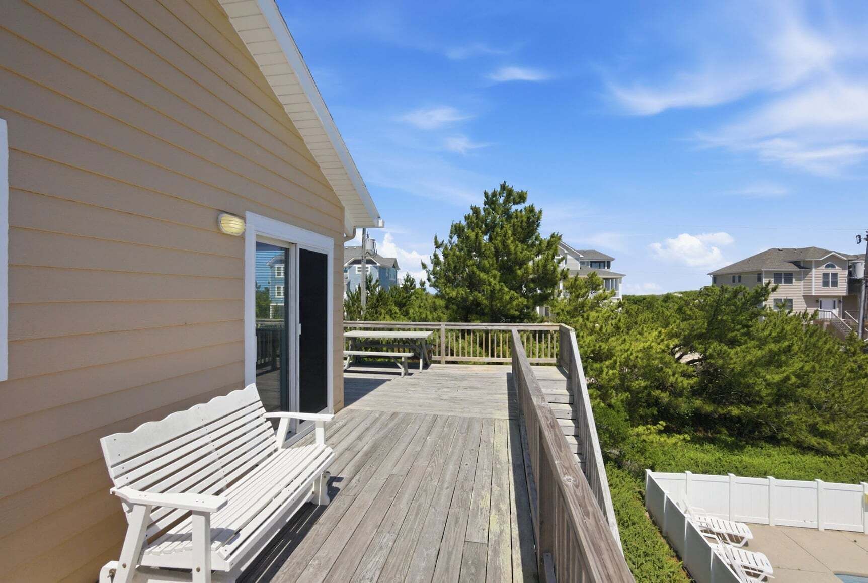 A wooden deck with a bench, a sliding glass door, and a view of a residential area with houses and trees.