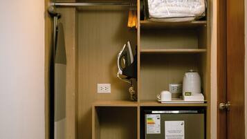A compact room with a wooden wardrobe, a small refrigerator, a coffee maker, and a shower curtain.