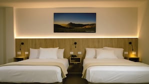 Habitación de hotel con dos camas, cabeceros de madera, lámparas de noche y un cuadro de paisaje enmarcado en la pared.