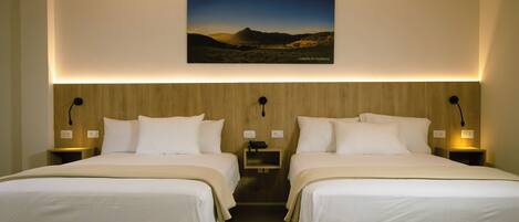 A hotel room with two beds, a wooden headboard, bedside lamps, and a framed landscape picture on the wall.