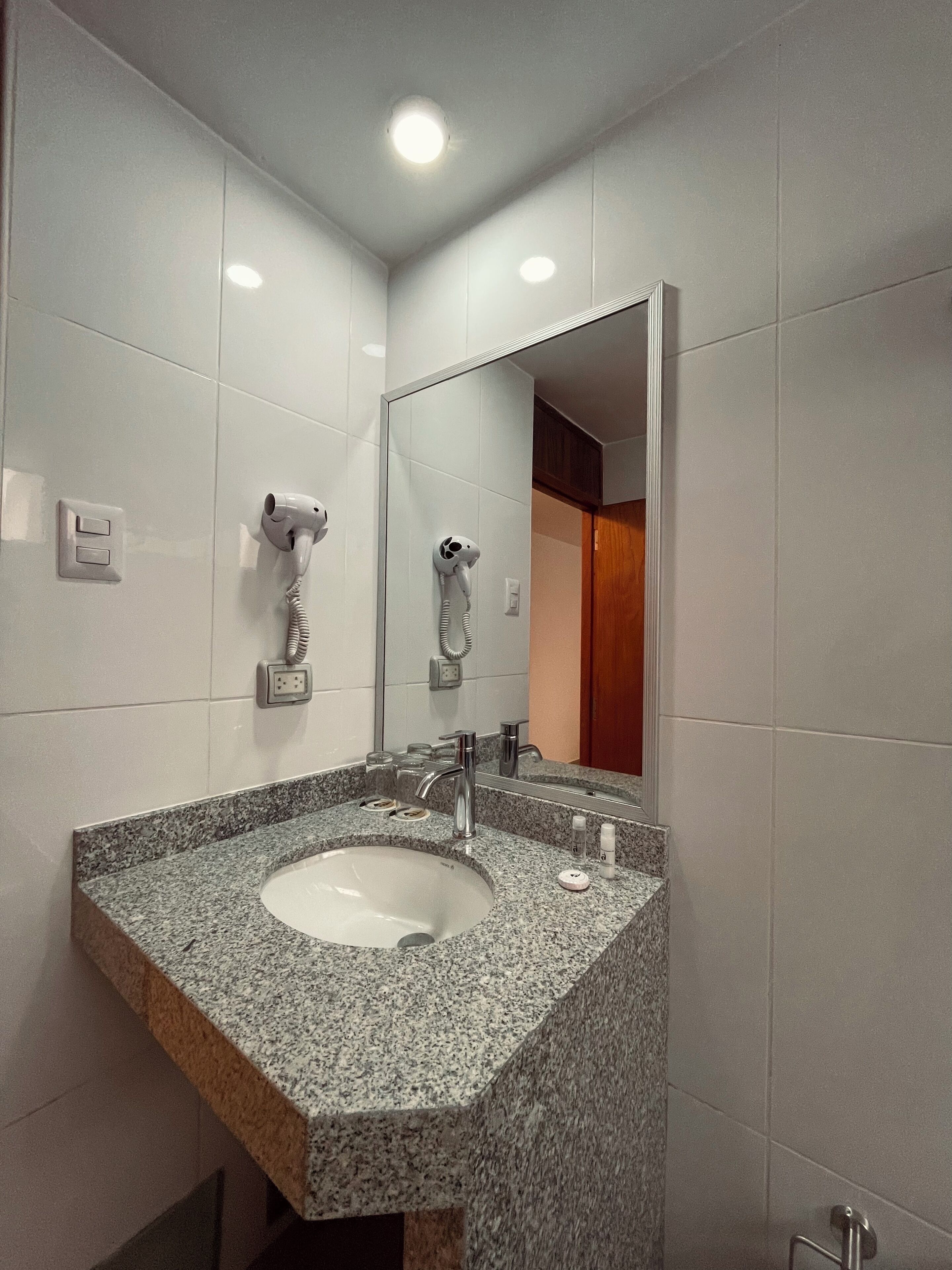A bathroom with a granite countertop sink, a mirror, and a hairdryer mounted on the wall.