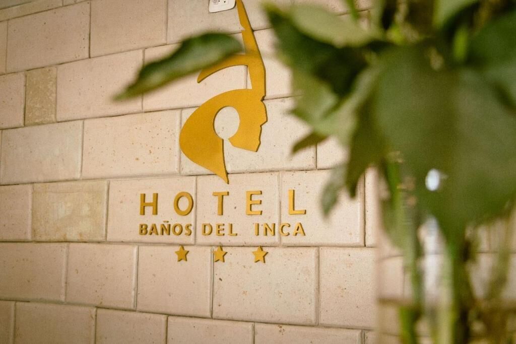 Skilt på en væg for Hotel Banos del Inca med en stiliseret silhuetlogo af et hoved.