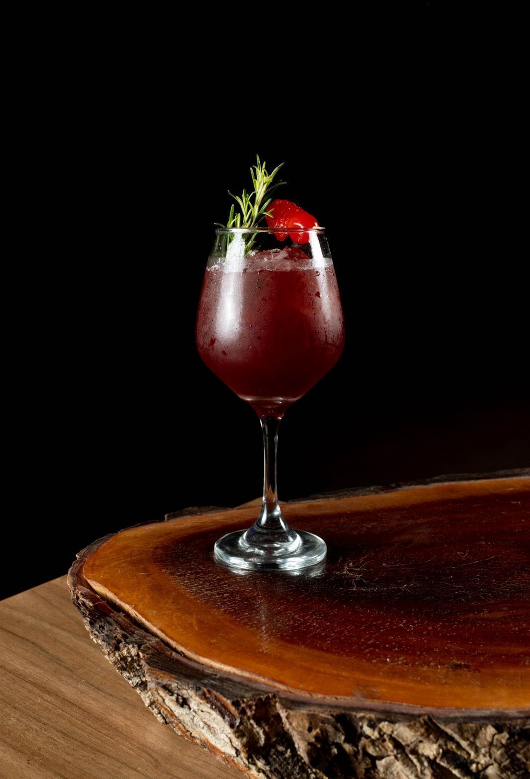 A glass of red beverage with a garnish on a wooden surface.