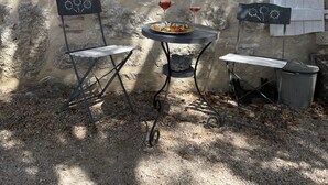 A stone wall with a white door, two metal chairs, a small table with a plate of food and two wine glasses, and a shelf with pinecones. - Magnifique Propriété sur un Terrain de 55 Ares, Piscine, 5 Chambres (Orniac)