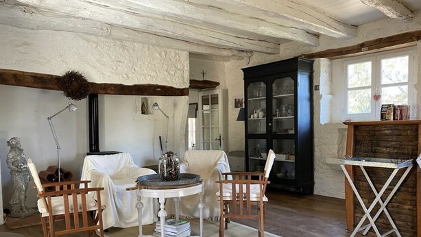 A rustic room with exposed wooden beams, a round table with chairs, a cabinet with glass doors, and a window with natural light. - Magnifique Propriété sur un Terrain de 55 Ares, Piscine, 5 Chambres (Orniac)