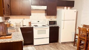 A compact kitchen with dark cabinets, a white stove, a microwave, and a refrigerator. - welcome to the soonerschooner (Norman)
