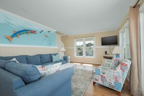 Un salon comprenant un canapé, un fauteuil à motifs, un téléviseur et une fresque représentant des poissons sur le mur.