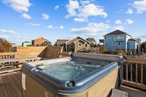 Un bain à remous sur une terrasse en bois, avec des maisons visibles au loin.