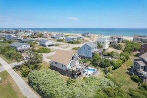 A coastal residential area with houses, a swimming pool, and a beach in the background.