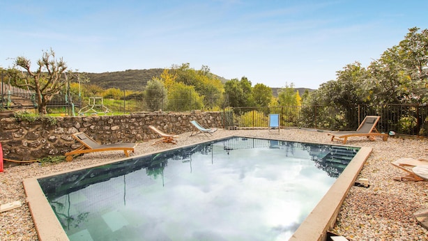 A rectangular swimming pool with a stone wall and a clear view of the surrounding landscape. - Stunning home in Darbres (Darbres)