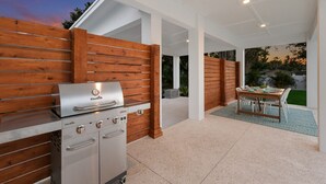 An outdoor kitchen area with a Char-Broil grill and a built-in oven, surrounded by wooden panels and a glass enclosure. - 3BR Lux Home, Heated Pool, Fire Pit, Outdoor TV (Palmetto)