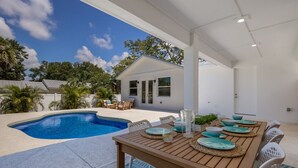 A poolside dining area with a table set for four, surrounded by chairs, and a view of a house in the background. - 3BR Lux Home, Heated Pool, Fire Pit, Outdoor TV (Palmetto)