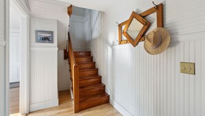 A wooden staircase with white paneling walls, a framed mirror, and a straw hat hanging on the wall. - Kennebunk's Golf and Beach Haven (Kennebunk)
