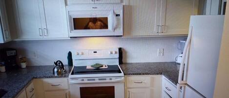 A kitchen with white cabinets, a microwave, an oven, and a refrigerator.