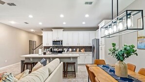 Une cuisine moderne avec des meubles blancs, un îlot central et un coin repas comprenant une table et des chaises en bois.