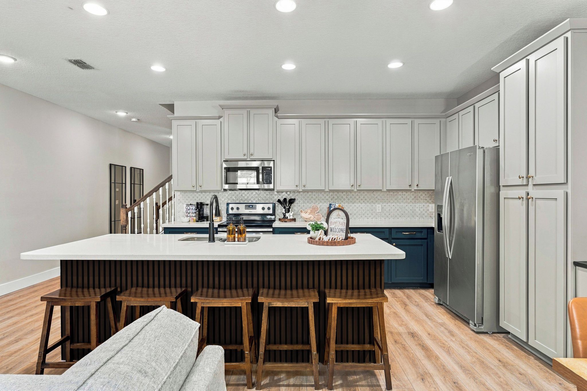 A modern kitchen with a large island, bar stools, a refrigerator, and a microwave.