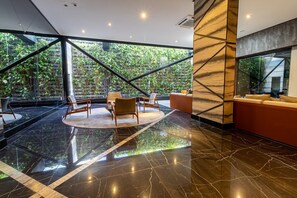 A modern lobby with a glass wall, a circular seating area, and a red sofa. - Time- melhor área de lazer de Maceio (Maceió)