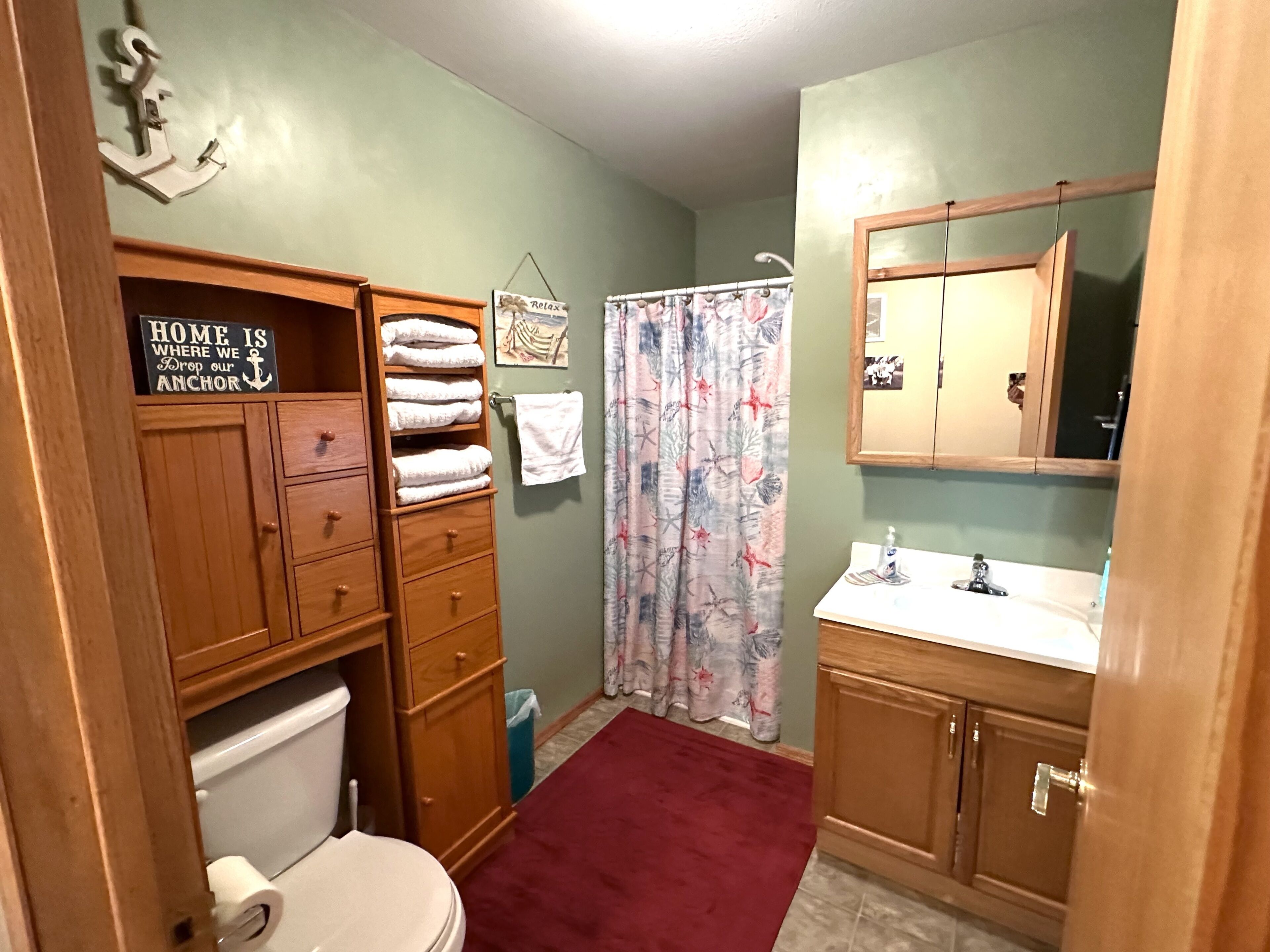 Une salle de bain avec des meubles en bois, des toilettes, un rideau de douche et un lavabo.