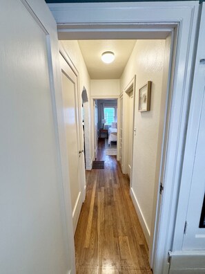 A hallway with wooden flooring, white walls, and a door leading to a bedroom. - Welcome to Tandem House! Family-Friendly, Southeast Portland Gem! (Portland)