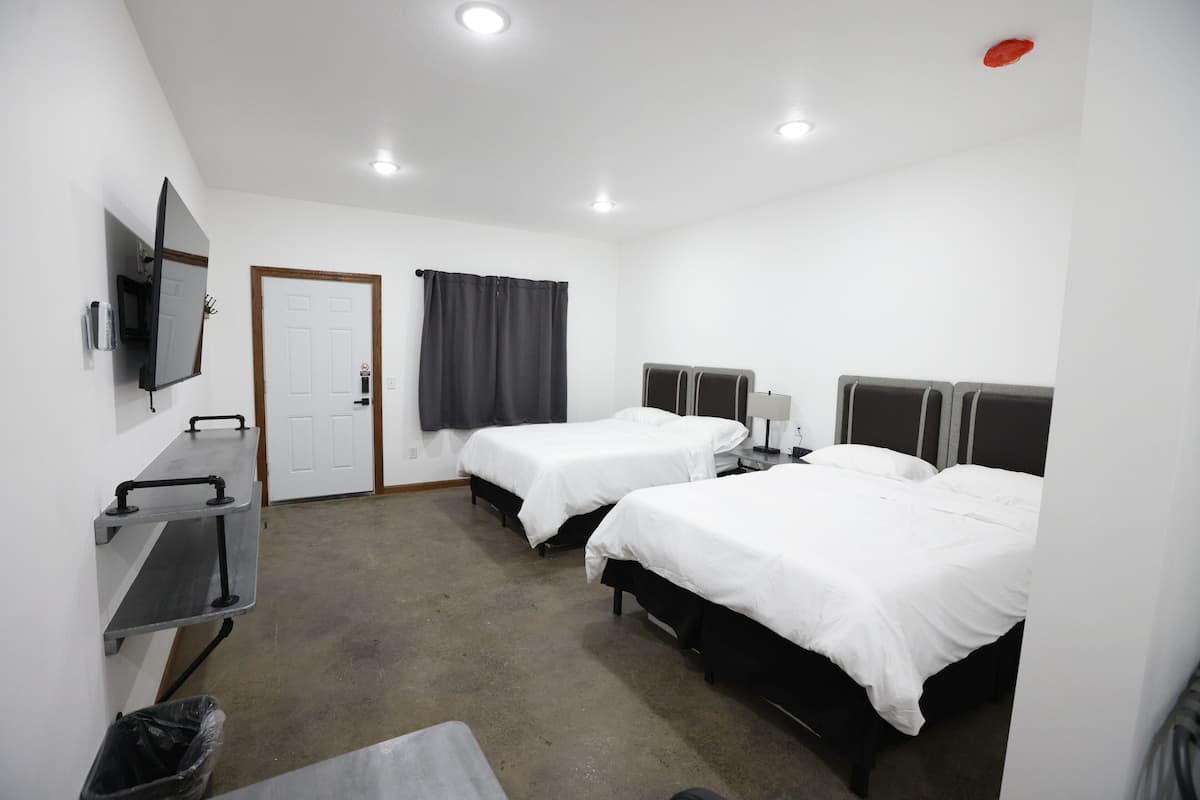 A hotel room with two single beds, a desk with a chair, a TV mounted on the wall, and a door with a curtain.