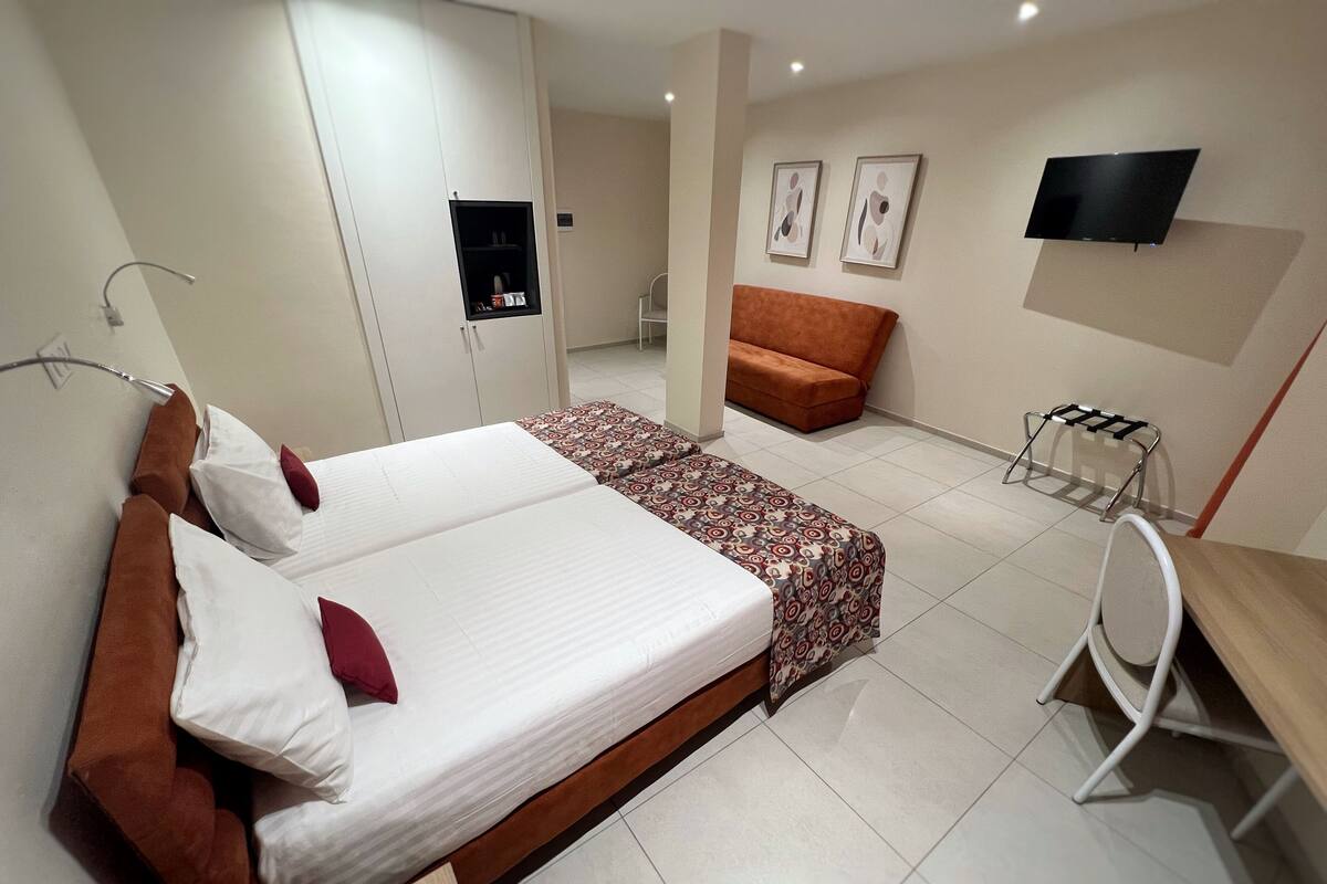 A hotel room with a large bed, a sofa, a desk, and a TV mounted on the wall.
