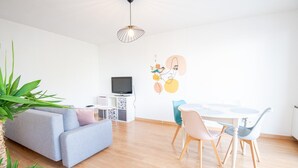 Un salon moderne comprenant un canapé, une table à manger avec des chaises, un téléviseur et un élément décoratif mural.