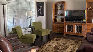 A living room with a brown leather sofa, green armchairs, a wooden entertainment center, and a TV. - Peaceful country farmhouse. Located 5 minutes from Historic downtown Post! (Post)
