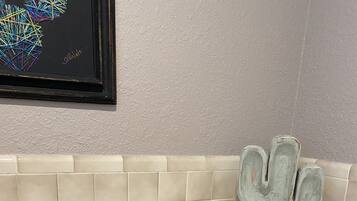 A bathroom with a toilet, a cactus decoration on the wall, and a shelf with towels.