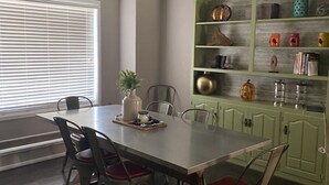 A dining area with a table and chairs, a window with blinds, and a green cabinet with various items. - Peaceful country farmhouse. Located 5 minutes from Historic downtown Post! (Post)